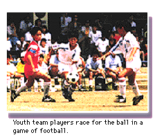 Youth team players race for the ball in a game of football.