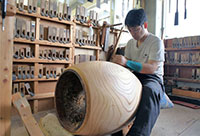 A man uses a plane carefully to shape the body of a wadaiko drum in the studio of Miyamoto-Unosuke Co. Ltd.