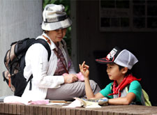 A boy counts syllables with his fingers to write a haiku as his grandmother looks on at Shinjuku Gyoen National Garden.