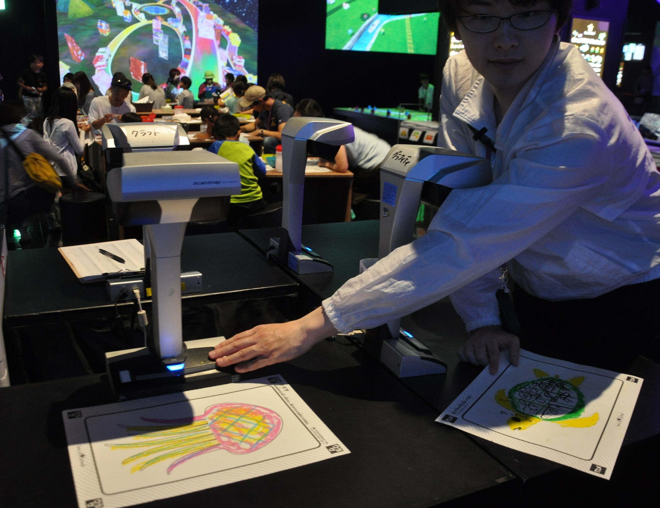  Miembro del personal escaneando dibujos de los niños en el ordenador – teamLab IsLands, Lalaport Shonan Hiratsuka