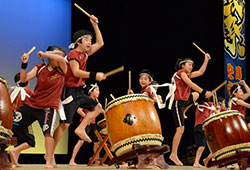 飛びはねながら長胴太鼓を乱れ打つ小学生のチーム（「太鼓祭」で）