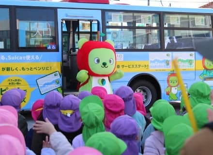 Nagano Prefecture’s bear mascot Arukuma greets children in front of a bus decorated with Arukuma illustrations. (Photo courtesy of Nagano Pref. PR Character, “Arukuma”)