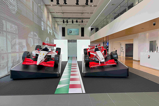 Two red-and-white Formula 1 race cars displayed on raised platforms inside a modern exhibition space.