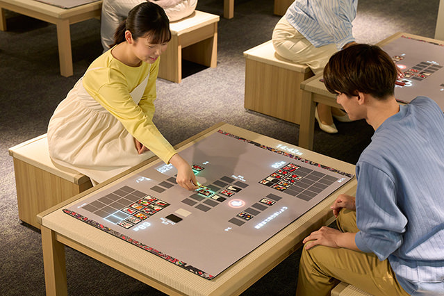 Two visitors seated at a large interactive table, playing a digital version of a traditional card game.
