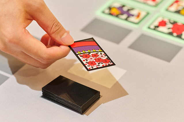 Close-up of a hand holding a colorful hanafuda card above a small stack of black cards on a tabletop.