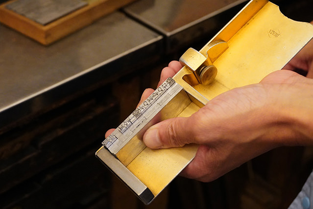 Close-up of hands adjusting metal type in a wooden letterpress composing stick.