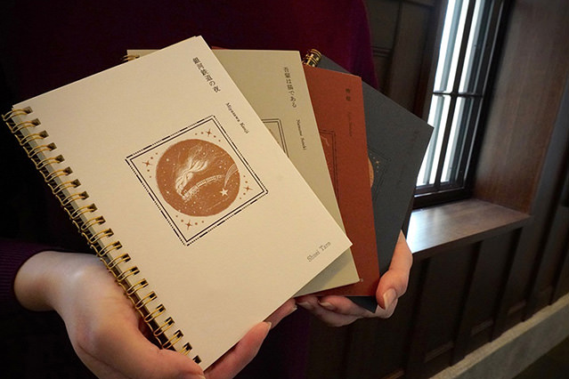 Person holding several spiral-bound notebooks with printed covers, stacked in their arms.